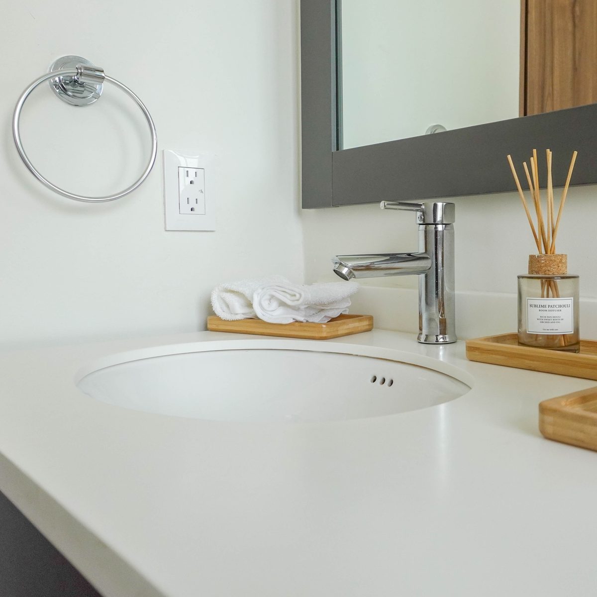 Lavabo del baño: cubierta blanca, grifo cromado, toallero de aro y espejo con marco gris
