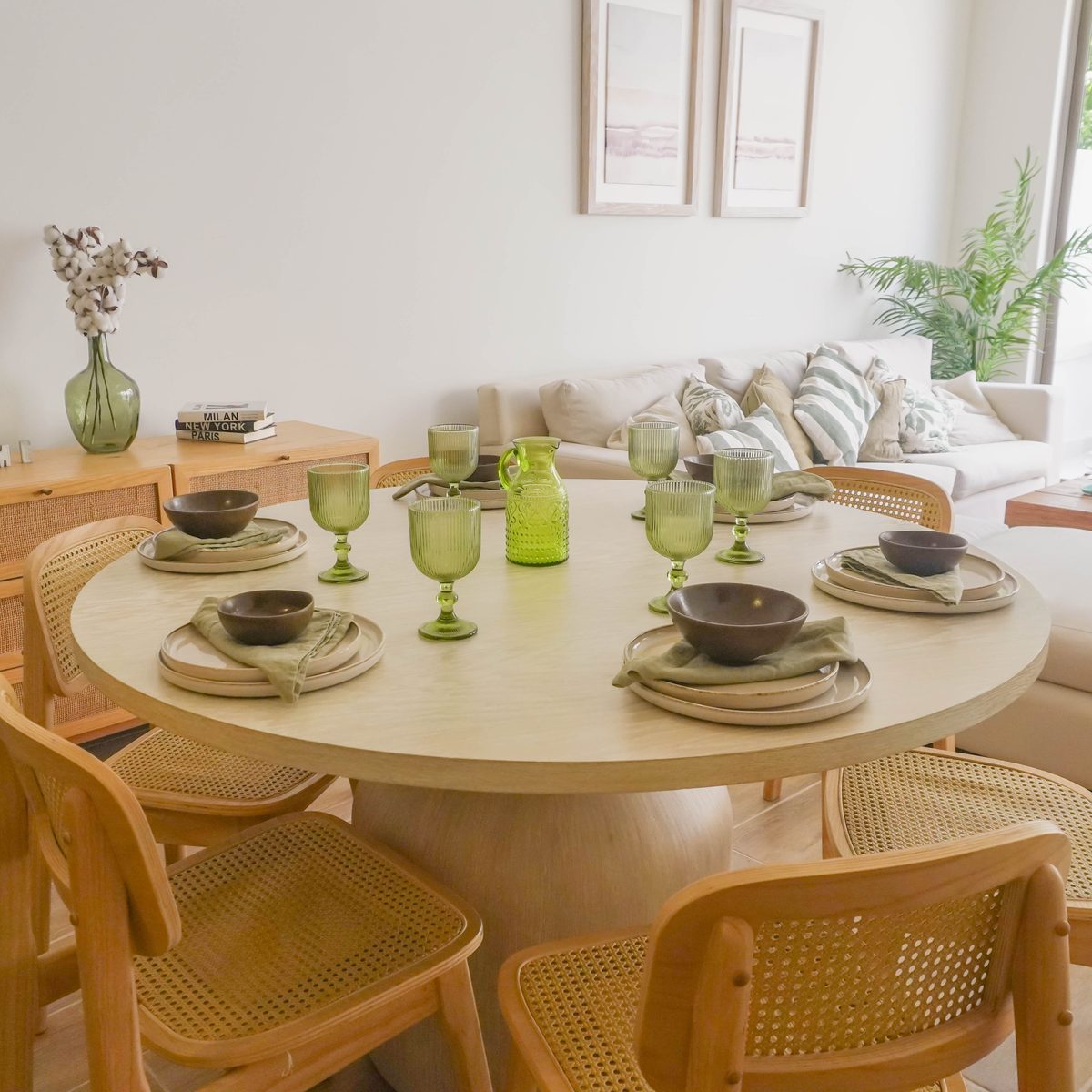 Mesa de comedor redonda con la mesa puesta y la sala al fondo