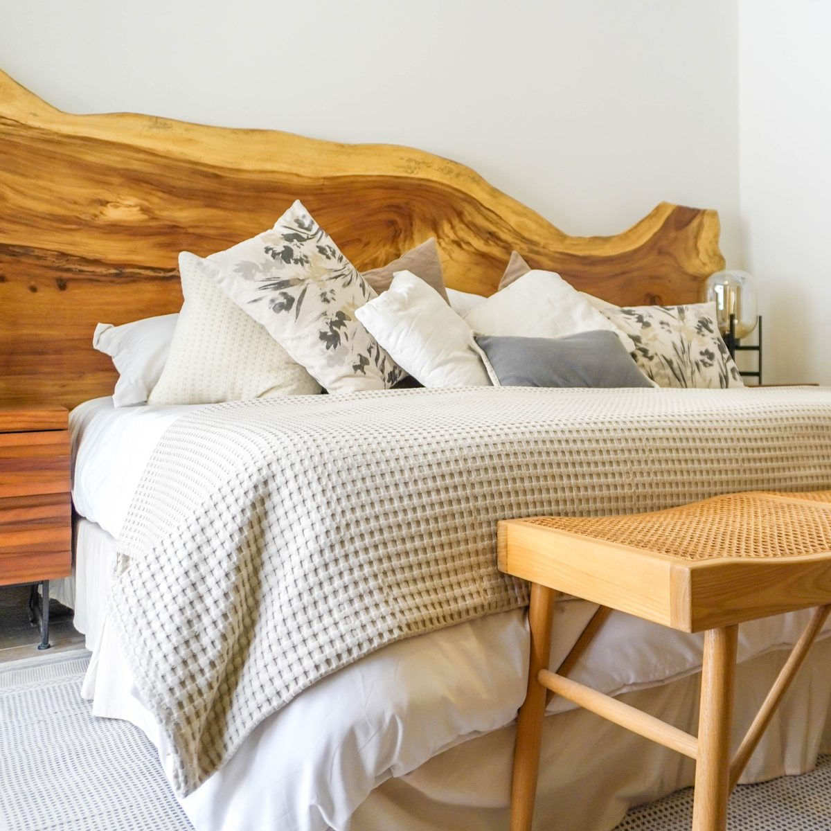Recámara principal del departamento muestra: cama con cabecera de madera de canto natural y banca de ratán al pie